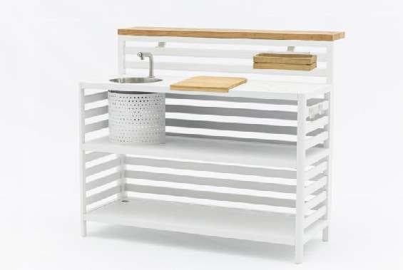 A white outdoor kitchen unit with a sink, faucet, and wooden cutting board, accompanied by a slatted white privacy screen.
